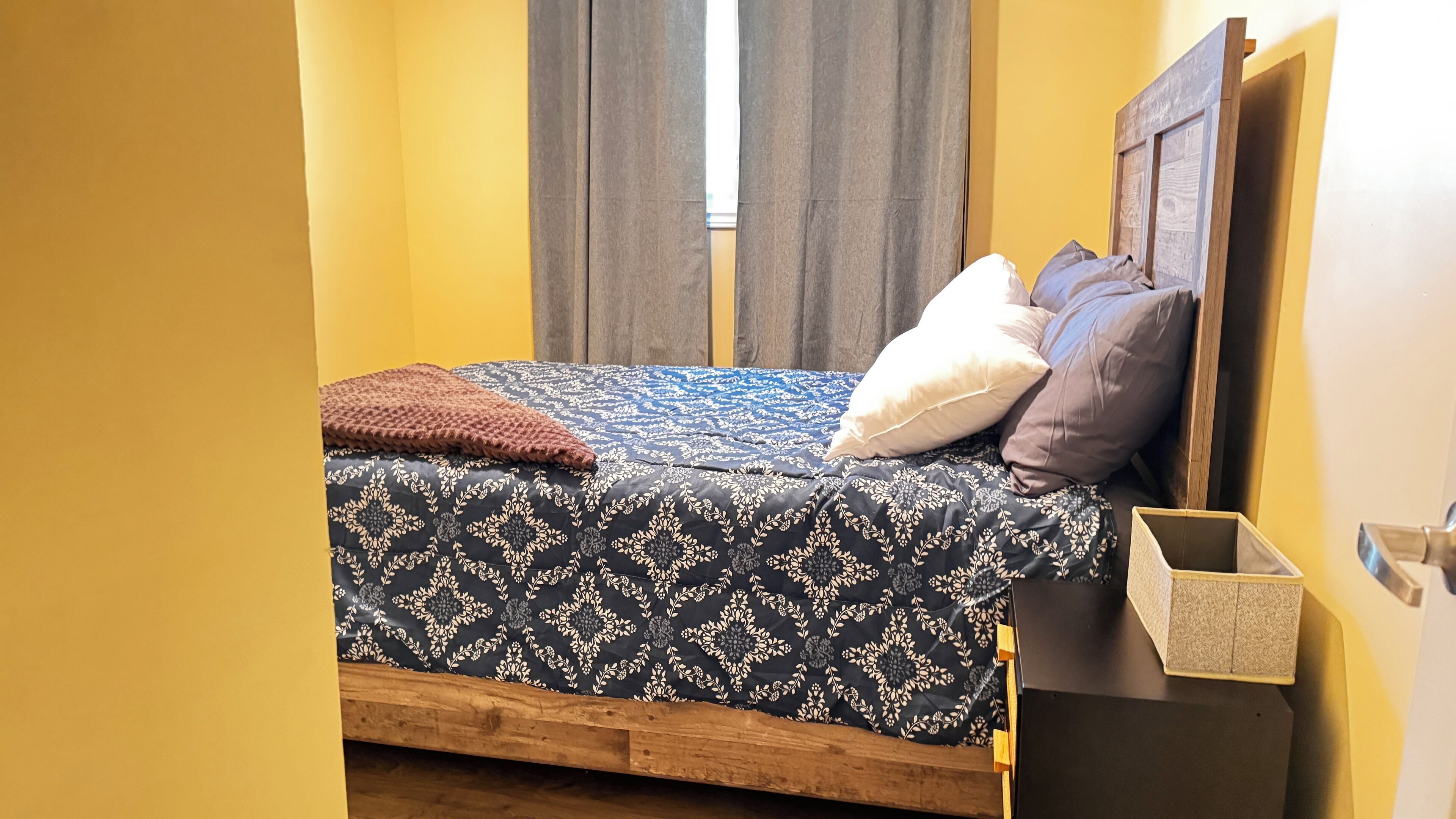 A bed with a patterned bedspread, pillows, and a brown throw.