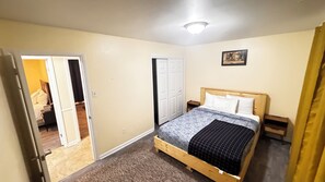 Una camera da letto con un letto, una porta, un comodino e un quadro appeso al muro.