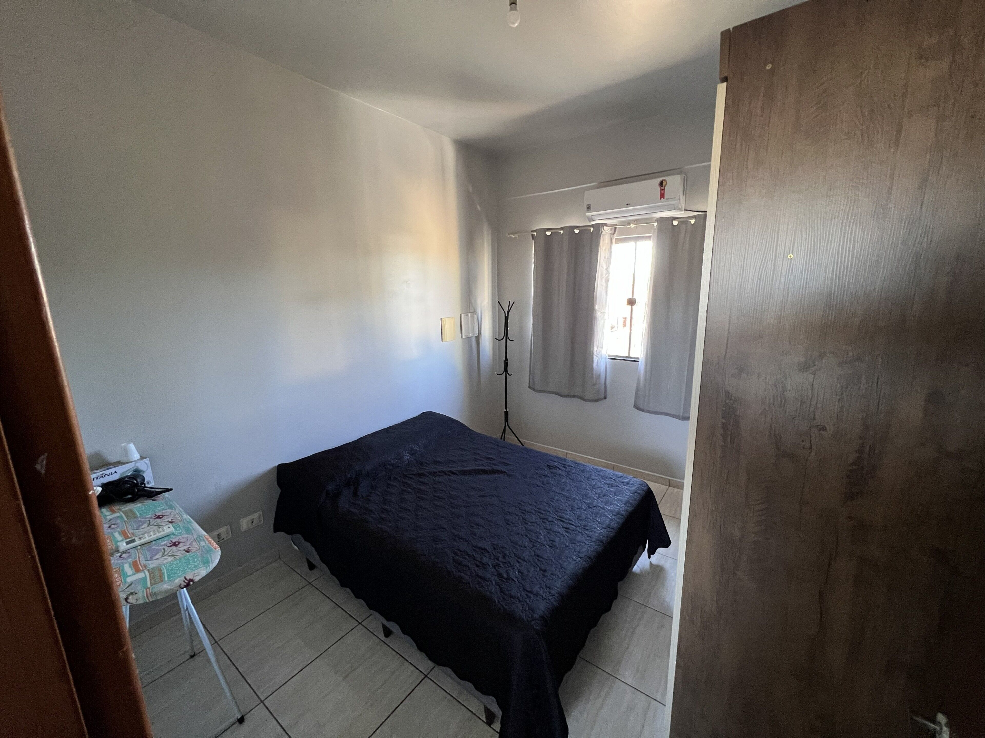 Una habitación pequeña y poco amoblada con una cama individual, una mesita y una ventana con cortinas.