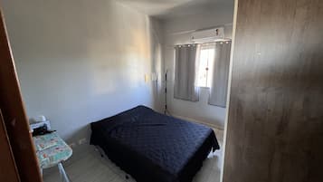 Una habitación pequeña y poco amoblada con una cama individual, una mesita y una ventana con cortinas.