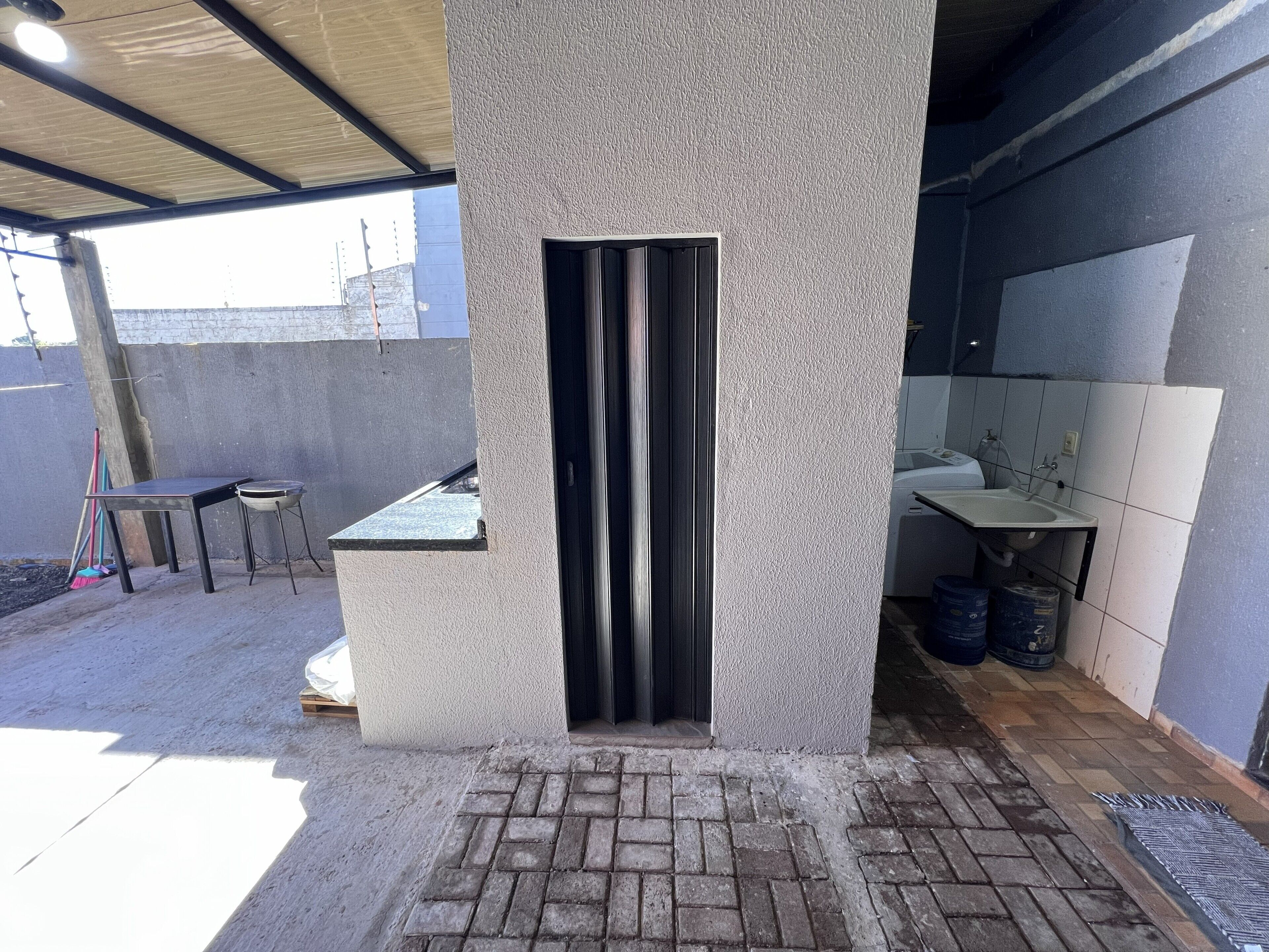 Un espacio al aire libre techado con piso de concreto, una mesa metálica y un banco.