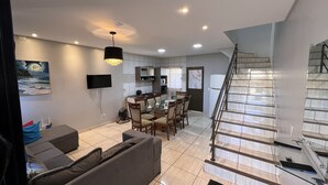 Ein modernes Wohnzimmer mit einer Couch, einem Esstisch mit Stühlen, einer Küchenzeile und einer Treppe.