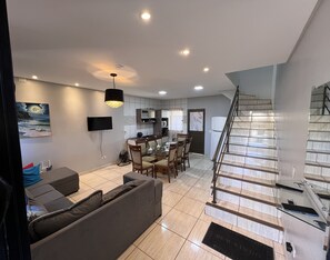 Una sala de estar moderna con sofá, una mesa de comedor con sillas, una zona de cocina y una escalera.