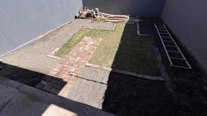Eine Dachterrasse mit befestigtem Bereich, einem Rasenstück und einer Leiter.