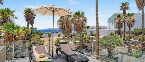 Una terraza en la azotea con sillones de sol, una sombrilla grande y palmeras.