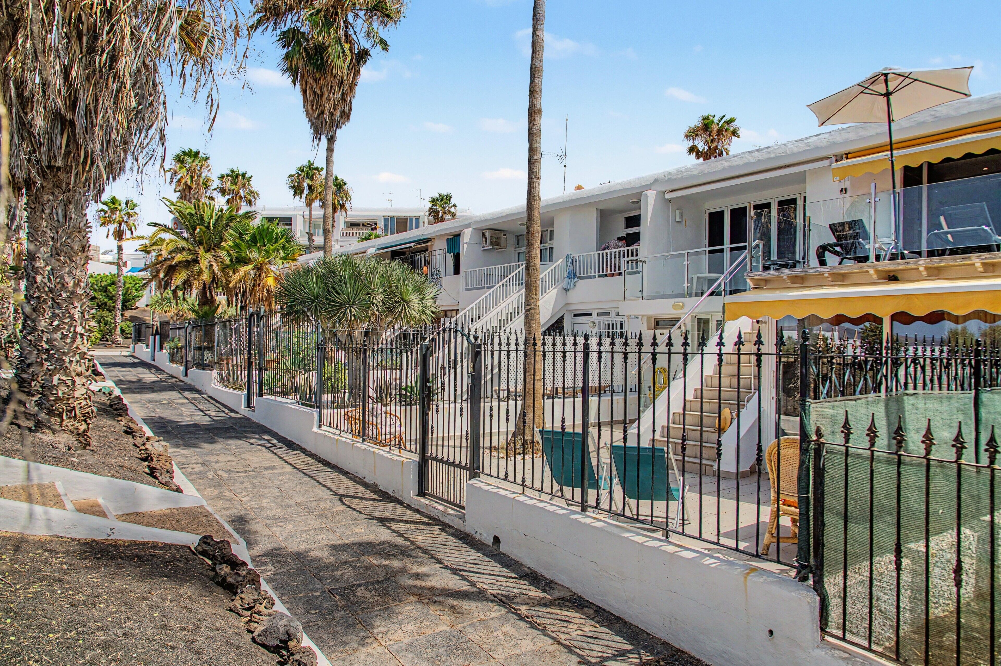 A residential area with a gated entrance, palm trees, and a building with a balcony.