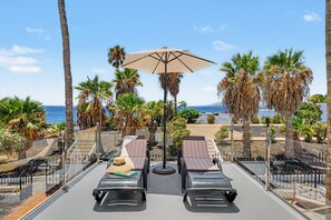 A balcony with two sun loungers, a large umbrella, and a view of the sea and palm trees. - Holiday Apartment 'Casa Sherazad' with Sea View, Private Terrace and Wi-Fi (Tías)
