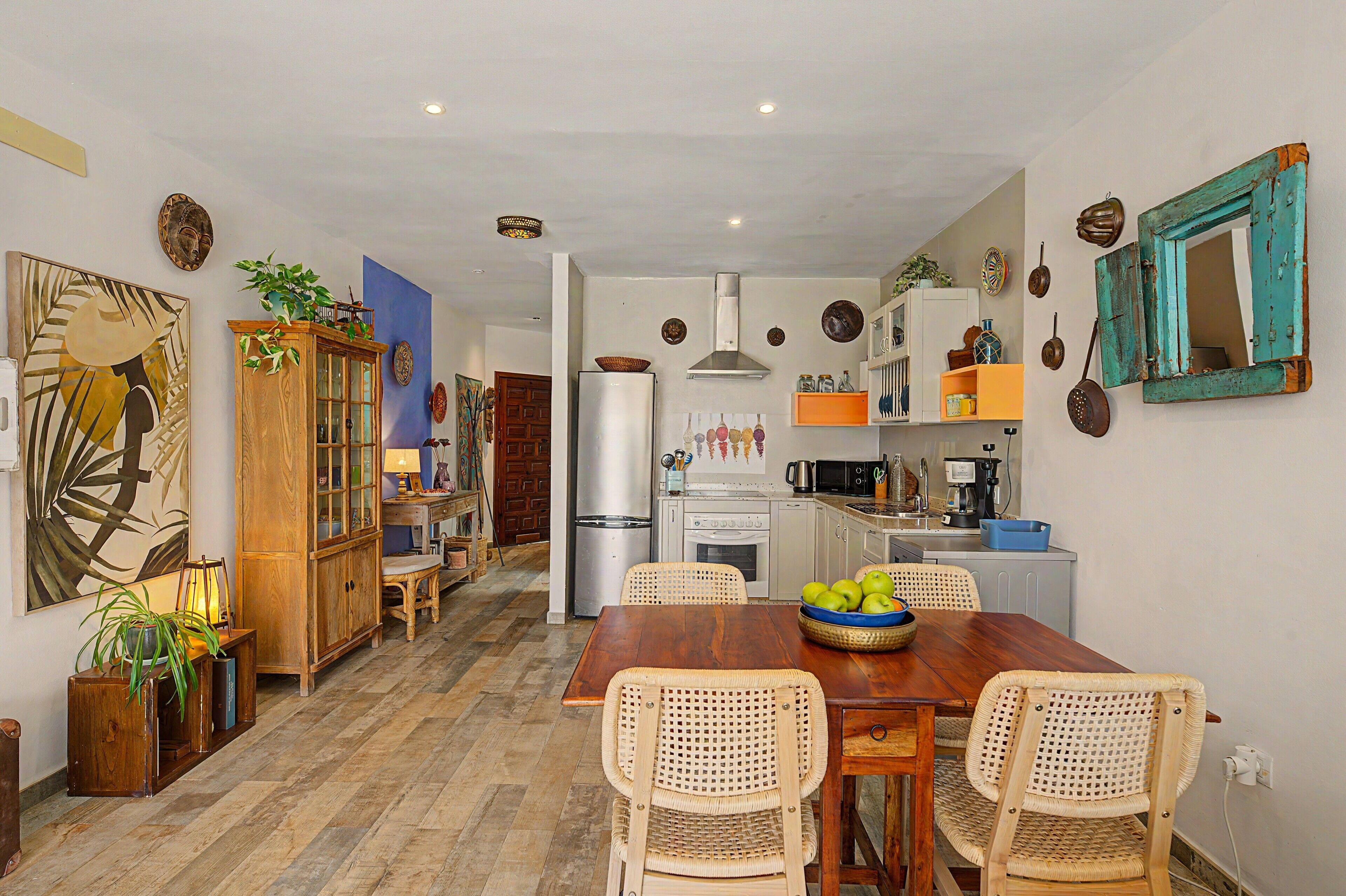A dining area with a wooden table and wicker chairs, a kitchen with modern appliances, and decorative wall art.
