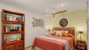 Un dormitorio con una cama, una estantería de madera, un ventilador de techo y una lámpara de pared.