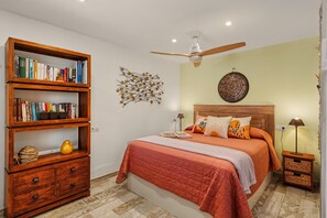 Un dormitorio con una cama, una estantería de madera, un ventilador de techo y una lámpara de pared.