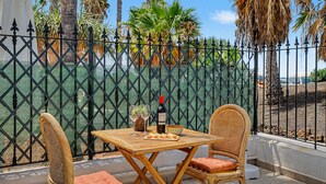 Un espacio al aire libre con sillas de mimbre y una mesa, una botella de vino y un tazón de aperitivos.