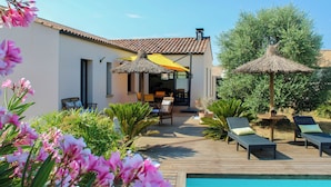 Eine Villa mit Pool, Sitzgelegenheiten im Freien und einem Strohdachschirm.