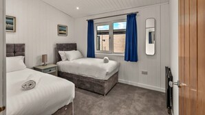 Un dormitorio con dos camas, una mesita de noche, una ventana con cortinas y un espejo en la pared.