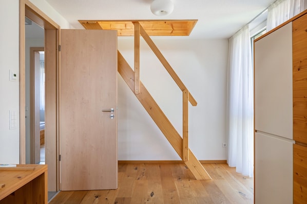 A room with a wooden staircase, a door, a small table, and a white wall.