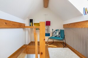 Ein Schlafzimmer im Loft-Stil mit geneigter Decke, Holzbalken, einem Türkis-Sessel, einem weißen Teppich und einem Bücherregal mit Büchern.