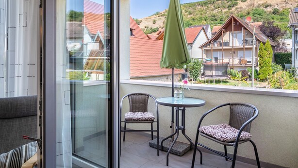 Un balcon avec deux fauteuils en osier, une petite table et un parasol vert.
