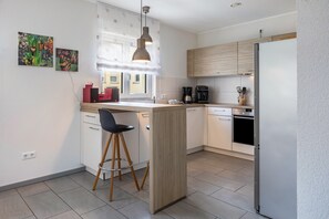 A modern kitchen with a central island, bar stools, a coffee machine, and a refrigerator. - Modern Holiday Home Paula with Pool at the Kaiserstuhl (Ihringen)