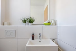 A bathroom with a white sink, a mirror, a green bowl, and two potted plants.