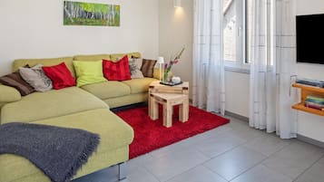 Ein modernes Wohnzimmer mit einem Ecksofa, einem kleinen Holztisch, einem roten Teppich und einem Gemälde an der Wand.