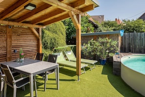 A covered outdoor area with a pool, a table with chairs, and lounge chairs.
