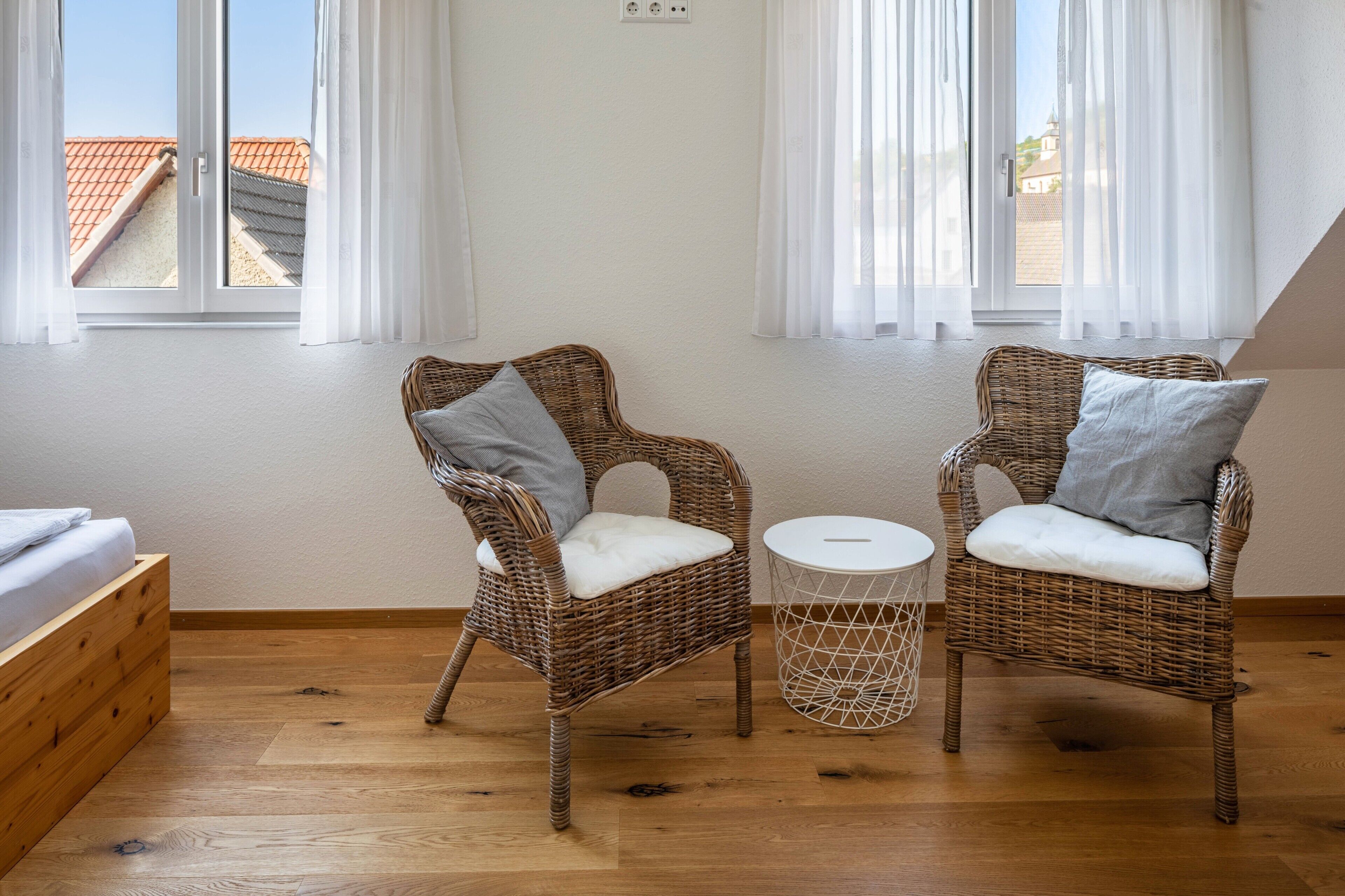 Ein Zimmer mit zwei Korbstühlen, einem kleinen runden Tisch und einem Bett.