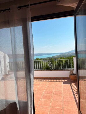 Uma varanda com vista para um lago e montanhas, piso de azulejos e guarda-corpo de metal.