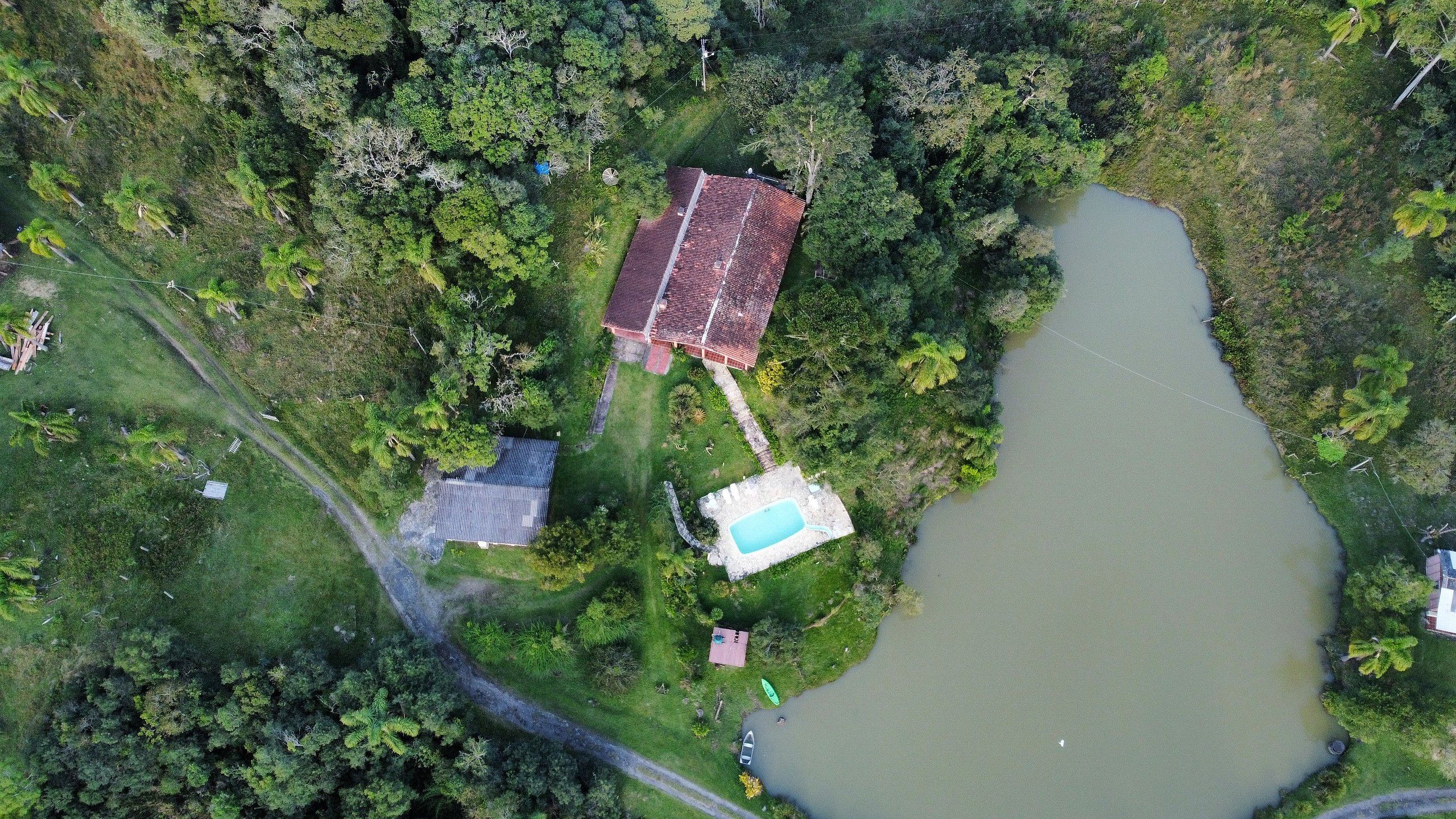 Vista aérea de una propiedad con piscina, un edificio de techo rojo y una construcción más pequeña.