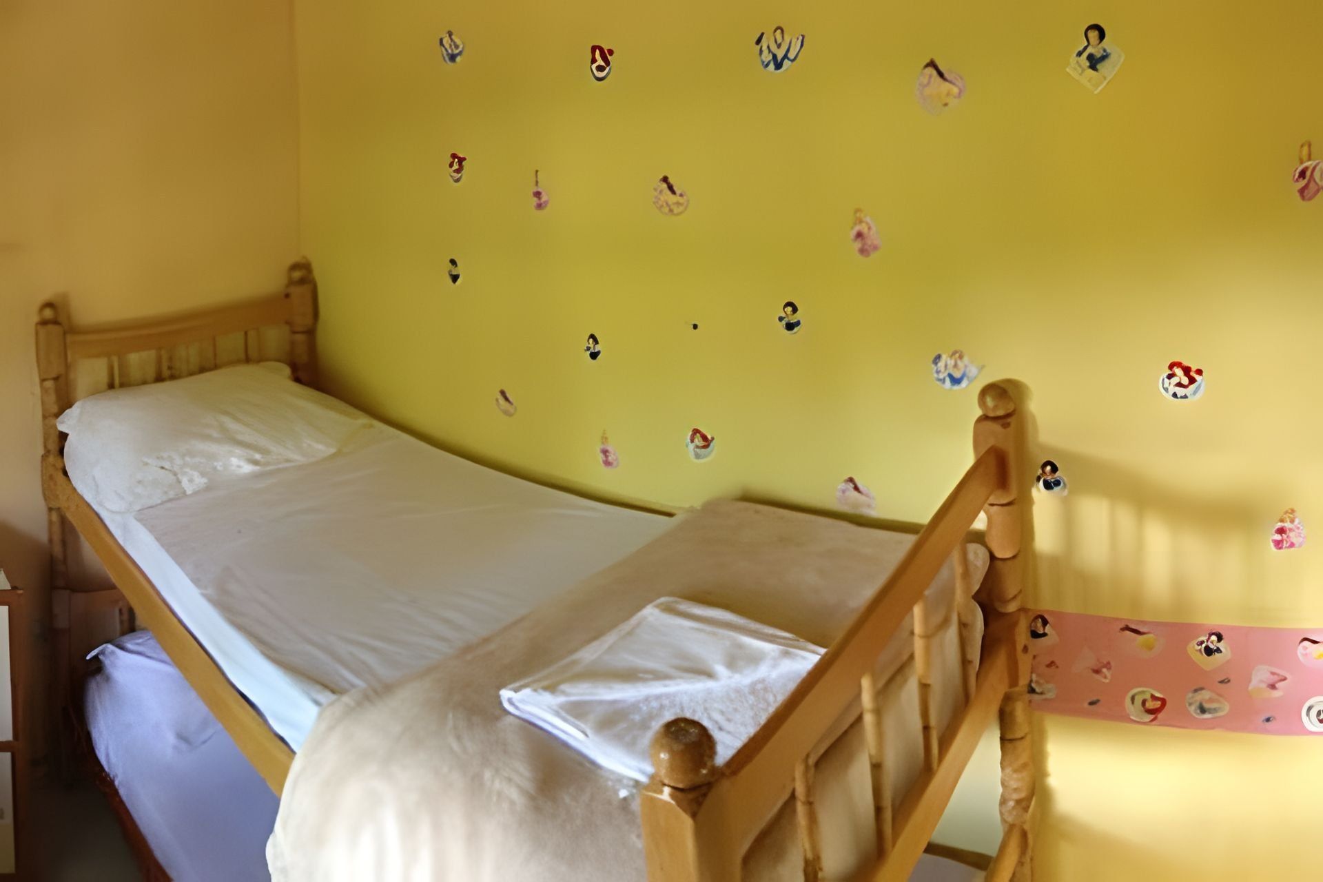 A single bed with a wooden frame and white bedding in a room with yellow walls.