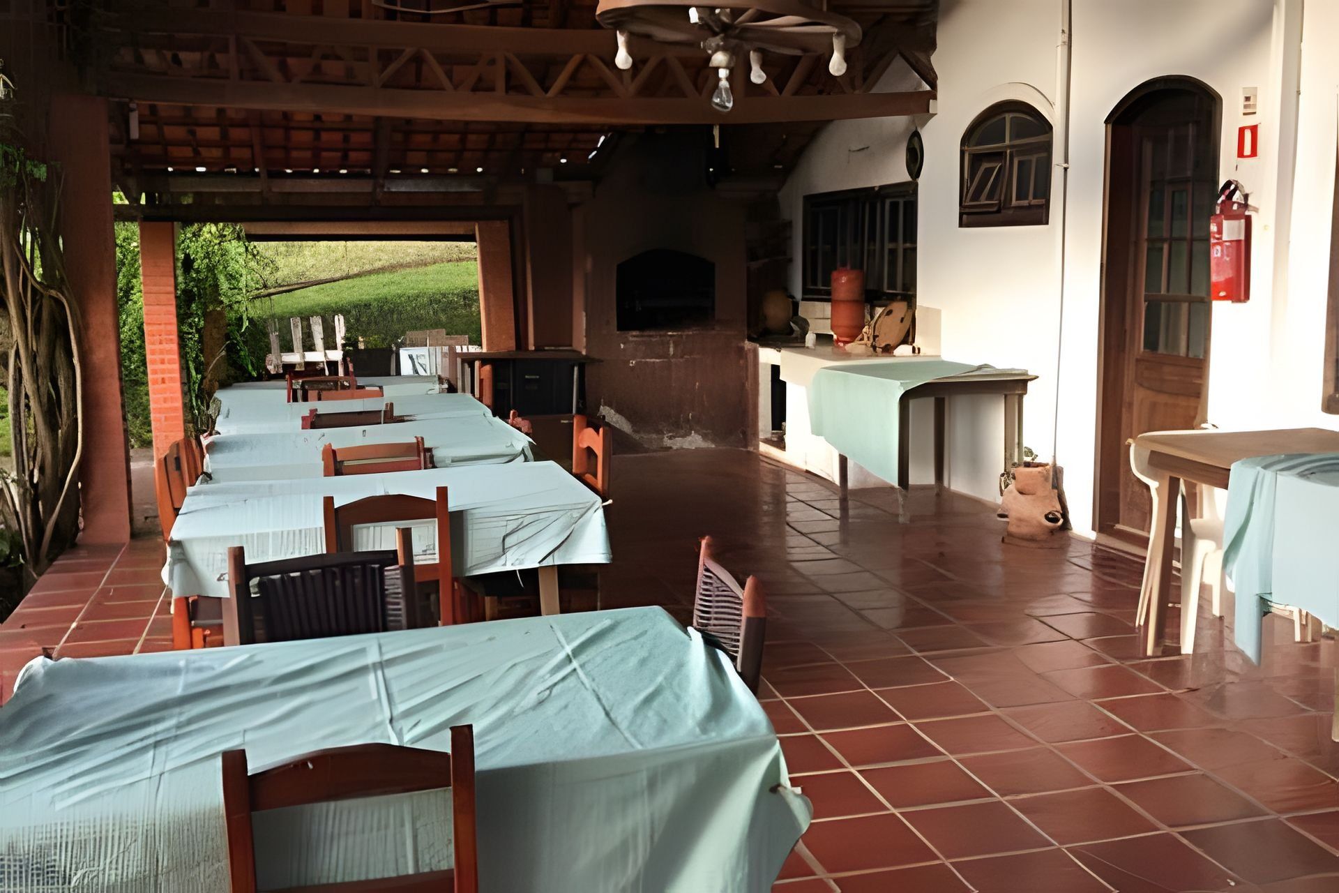 Un espacio de comedor al aire libre, cubierto, con varias mesas y sillas, una zona de cocina y vistas al exterior.