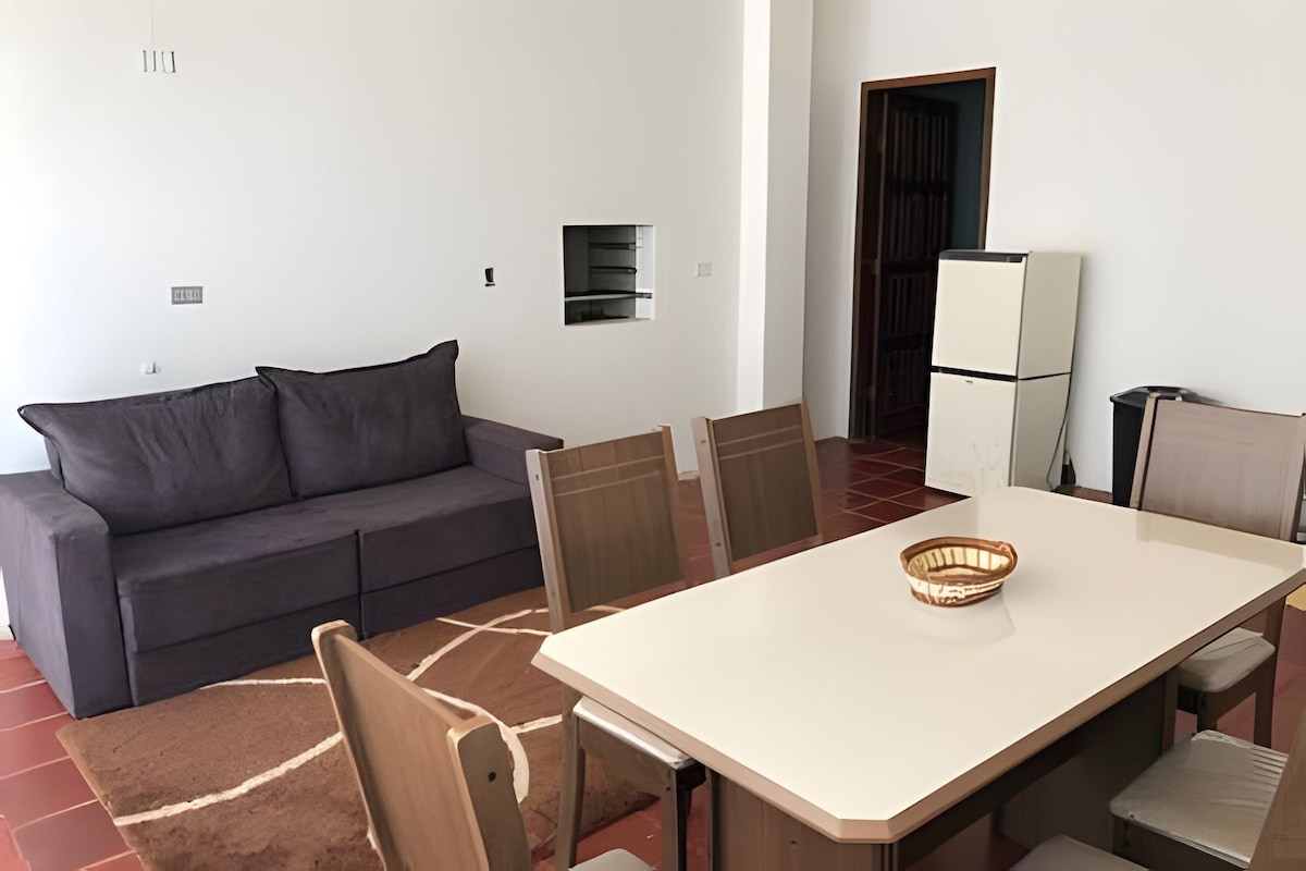 Un espace de vie compact comprenant un canapé, une table à manger, des chaises, un petit coin cuisine et un réfrigérateur.
