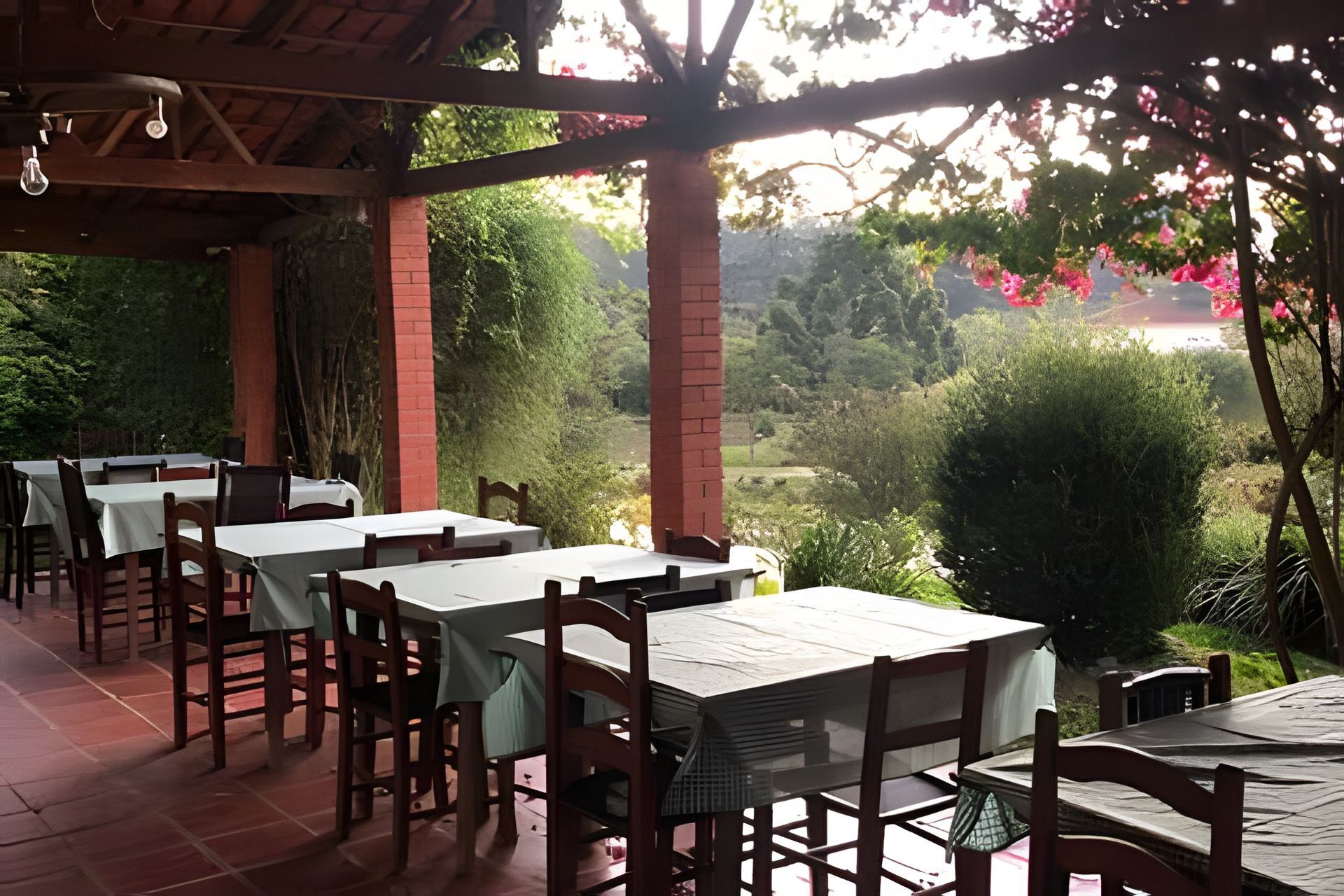 Un espacio de comedor al aire libre con mesas y sillas, un pilar de ladrillo y vistas a un jardín.