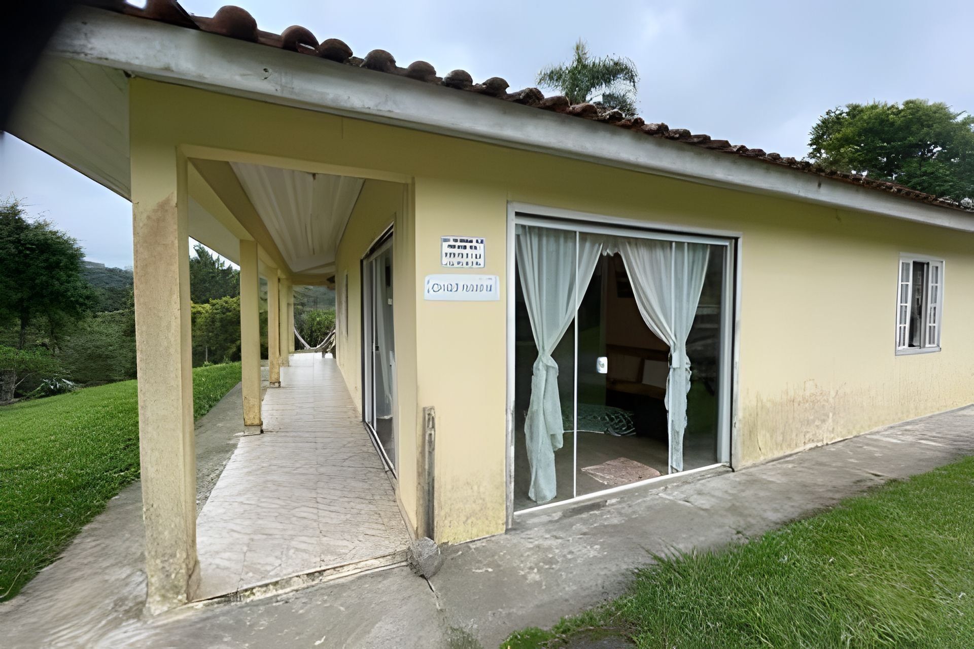 A building with a covered walkway, a door with curtains, and a sign.