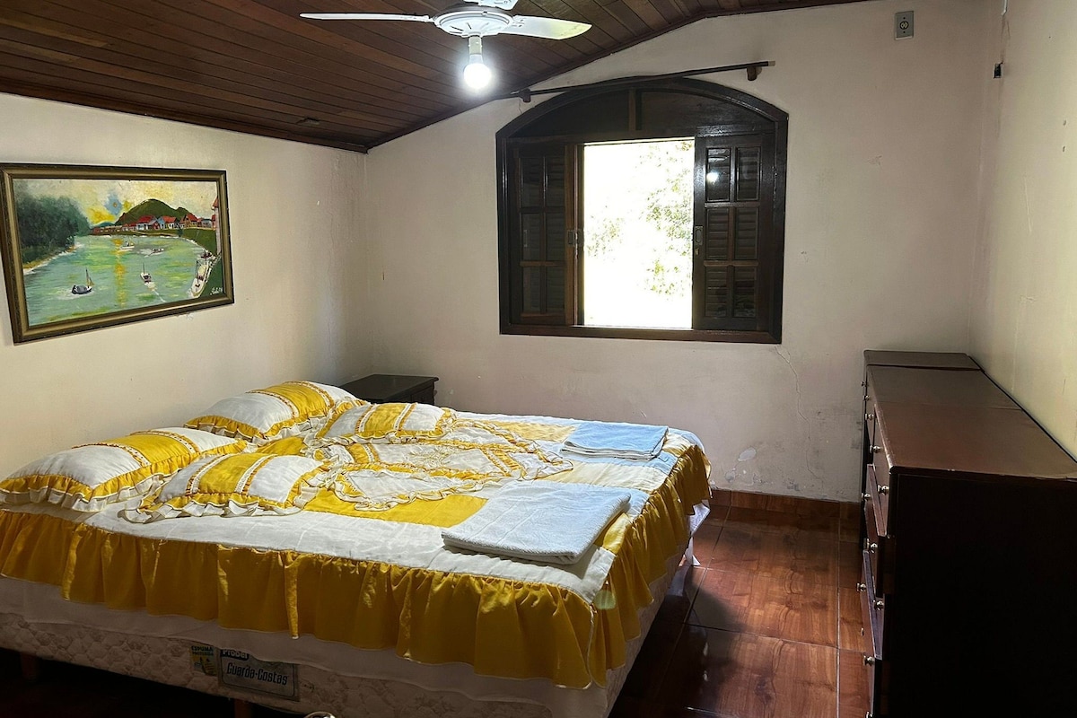 Une chambre à coucher avec un lit, un ventilateur de plafond, une fenêtre et un tableau accroché au mur.