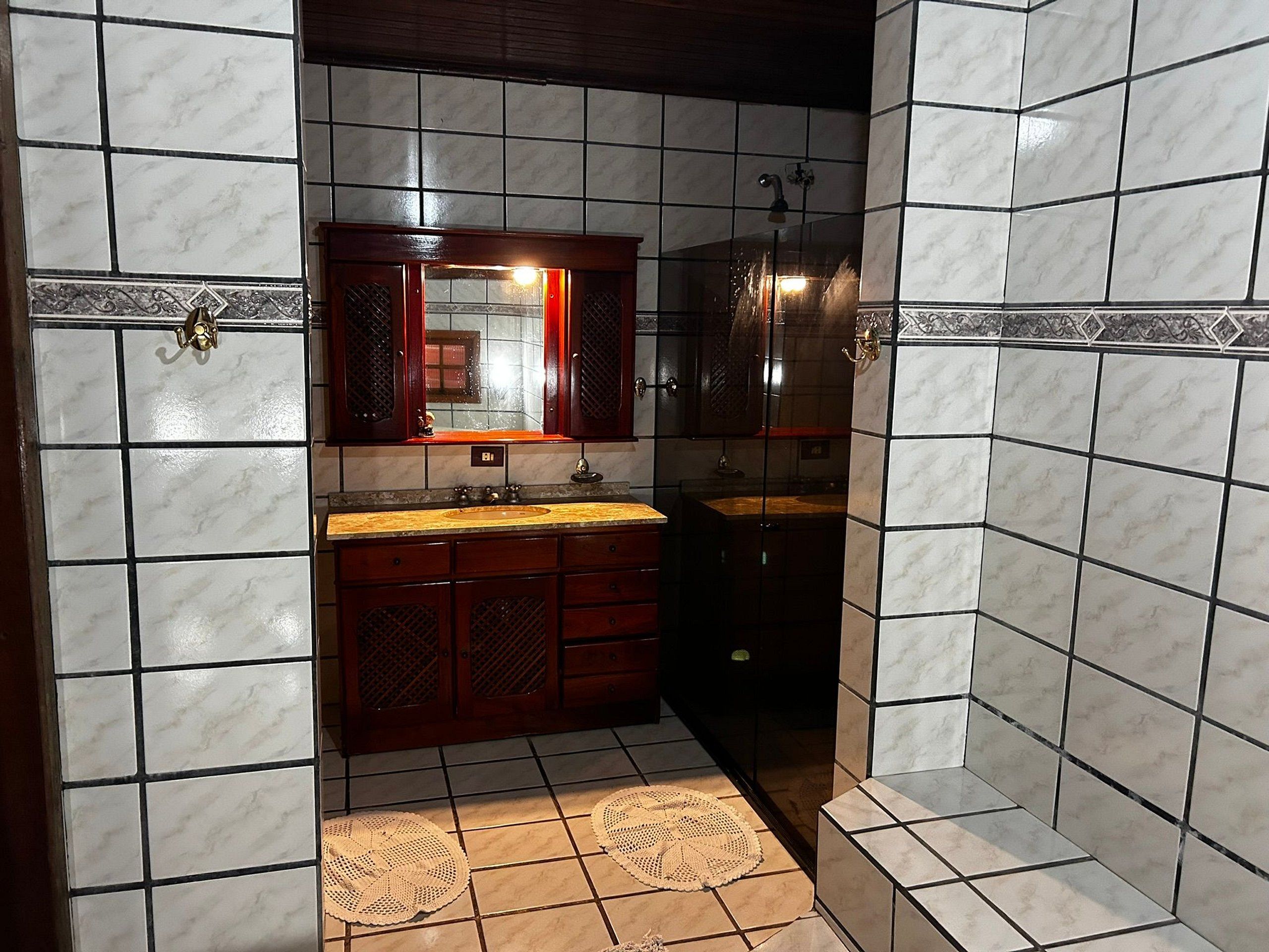 A bathroom with a marble-tiled wall, a wooden vanity with a sink, and a shower area.