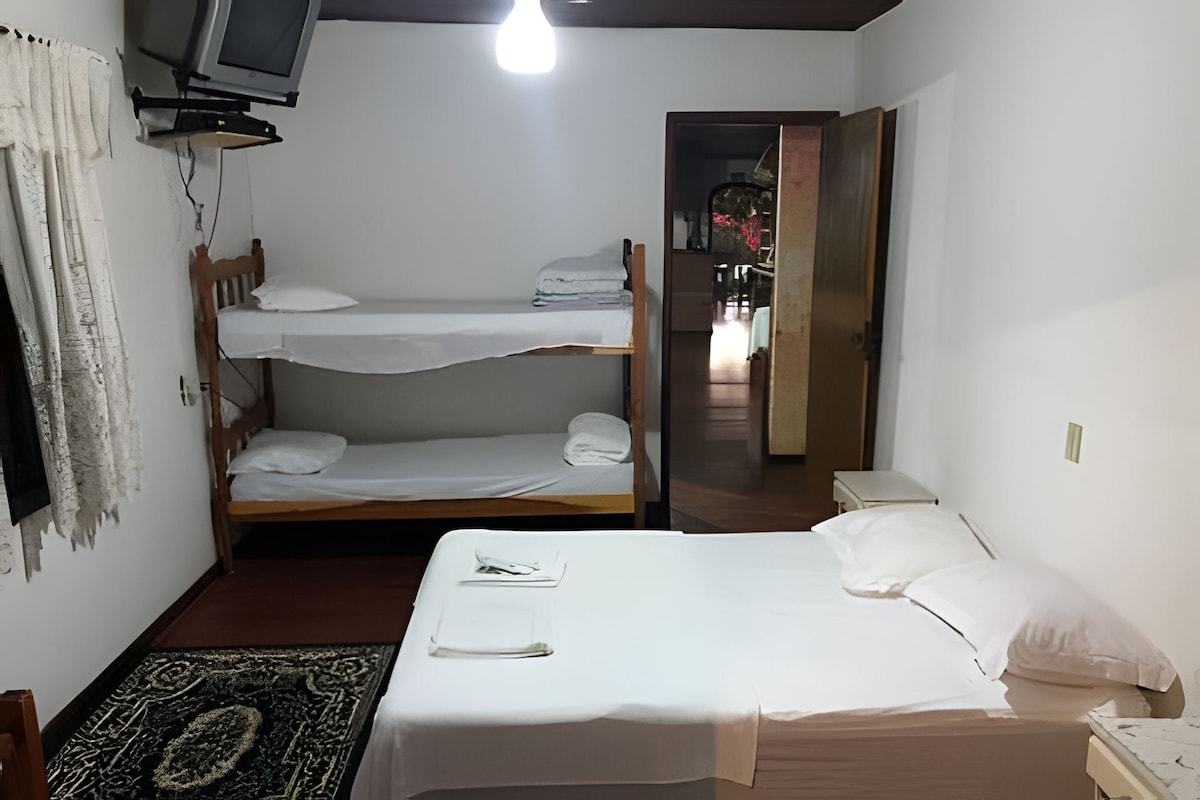 Quarto com beliches, escrivaninha, cadeira e televisão.