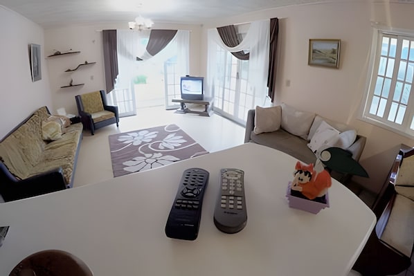 A living room with a sofa, a coffee table, and two remote controls on a white table.