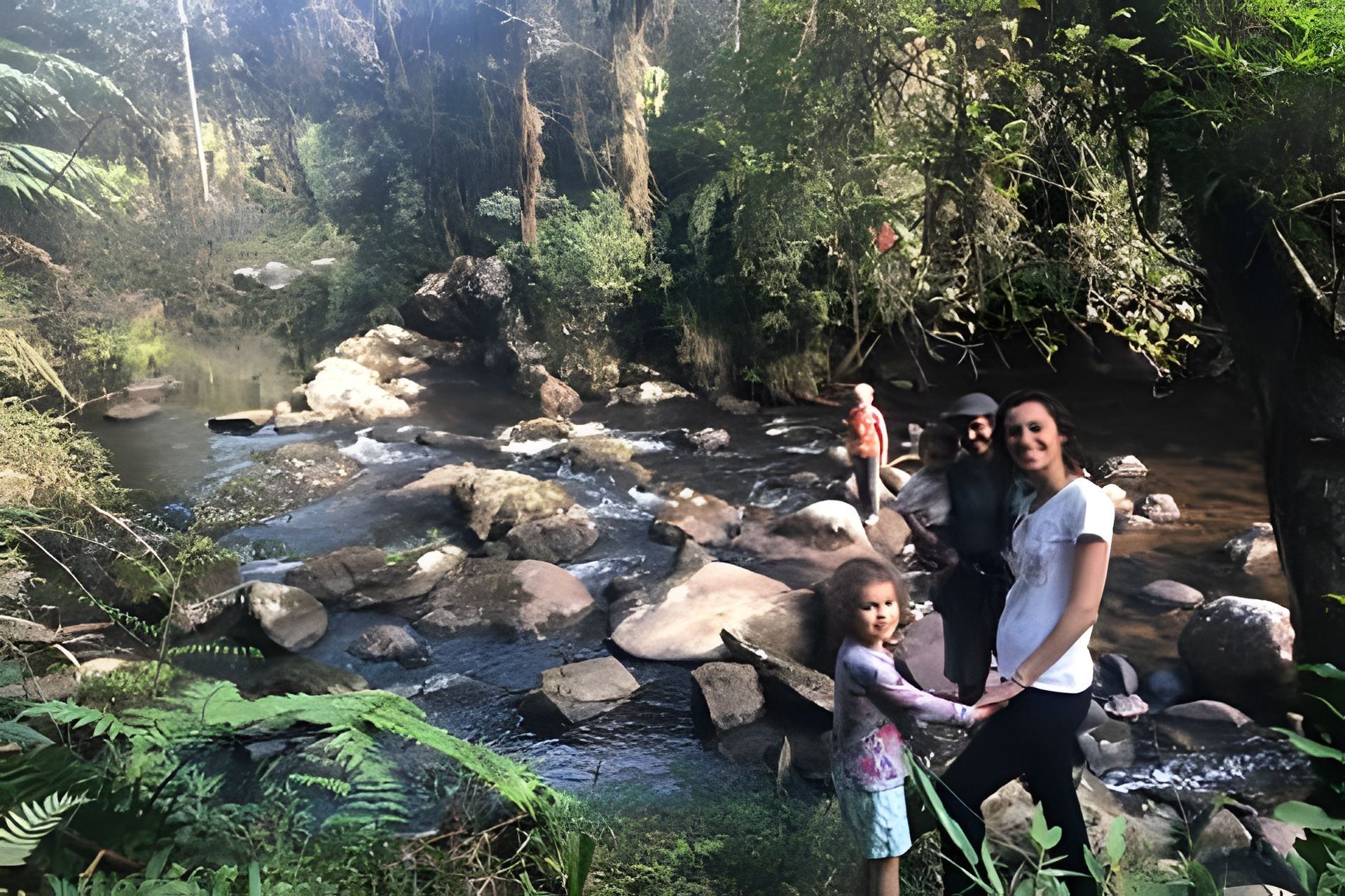 Une famille au bord d’un ruisseau rocheux, dans une zone boisée.