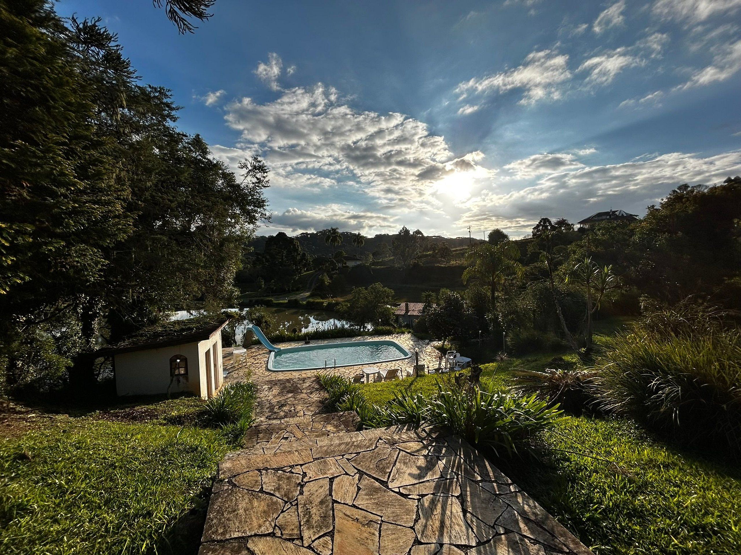 A stone pathway leading to a swimming pool surrounded by lush greenery and trees.