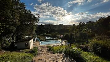 A stone pathway leading to a swimming pool surrounded by lush greenery and trees.