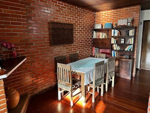 A room with a brick wall, a wooden table with chairs, a bookshelf, and a door.