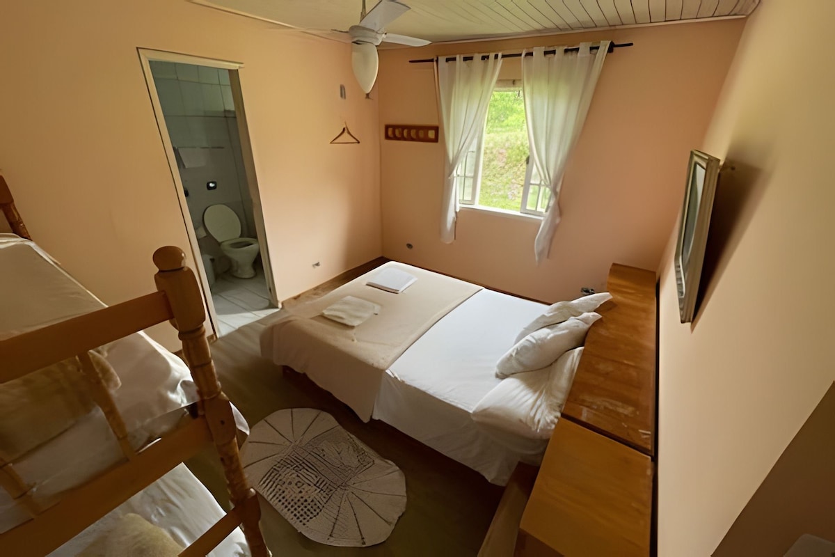 Une chambre avec un lit simple, une tête de lit en bois, une table de chevet, une fenêtre avec des rideaux et une vue sur l’extérieur.