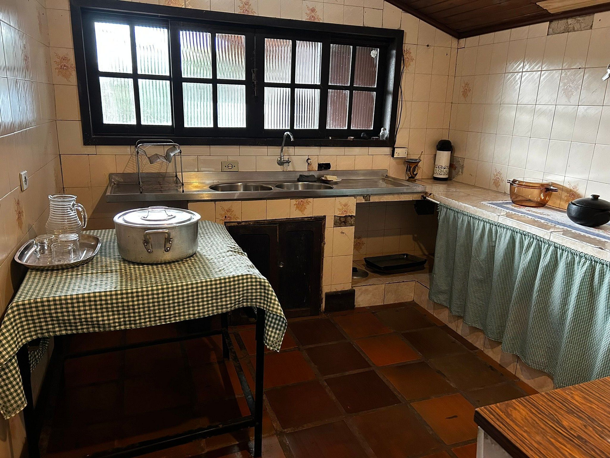 Une cuisine avec une fenêtre, un évier, une cuisinière et une table recouverte d’une nappe à carreaux.