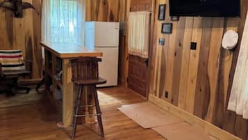 Un interno in legno con angolo cottura, uno sgabello da bar, un frigorifero e una televisione a parete.