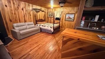 A wooden-paneled room with a bed, a sofa, a wooden table, and a kitchen area with a sink.