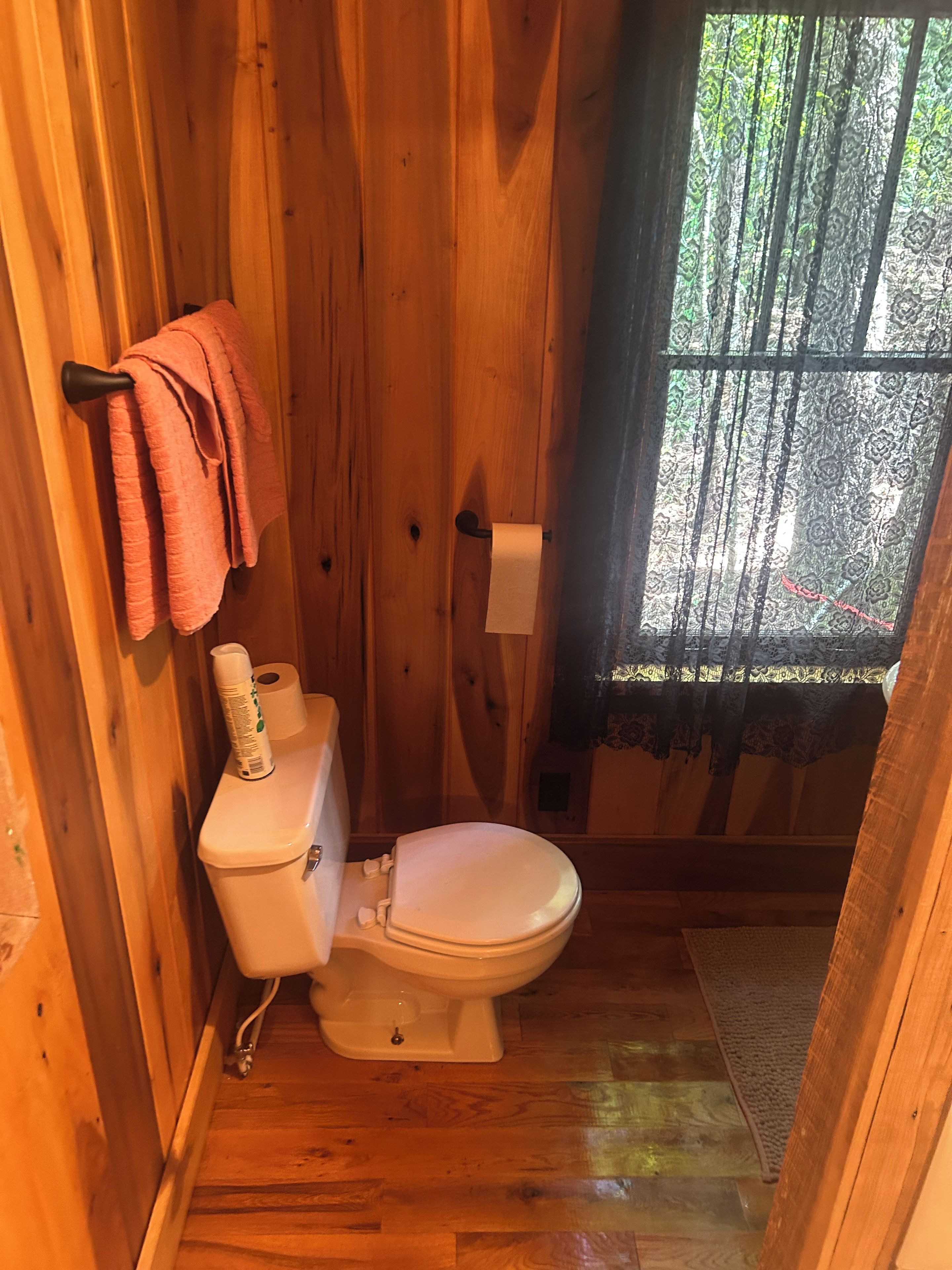Un baño de madera con inodoro, un rollo de papel higiénico y un perchero con toallas.