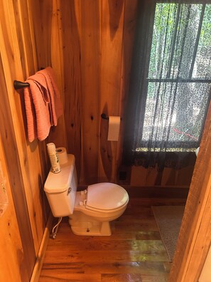 Un baño de madera con inodoro, un rollo de papel higiénico y un perchero con toallas.