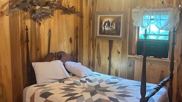 Camera da letto in una baita di legno, con un letto, un quadro incorniciato e una finestra con tende.
