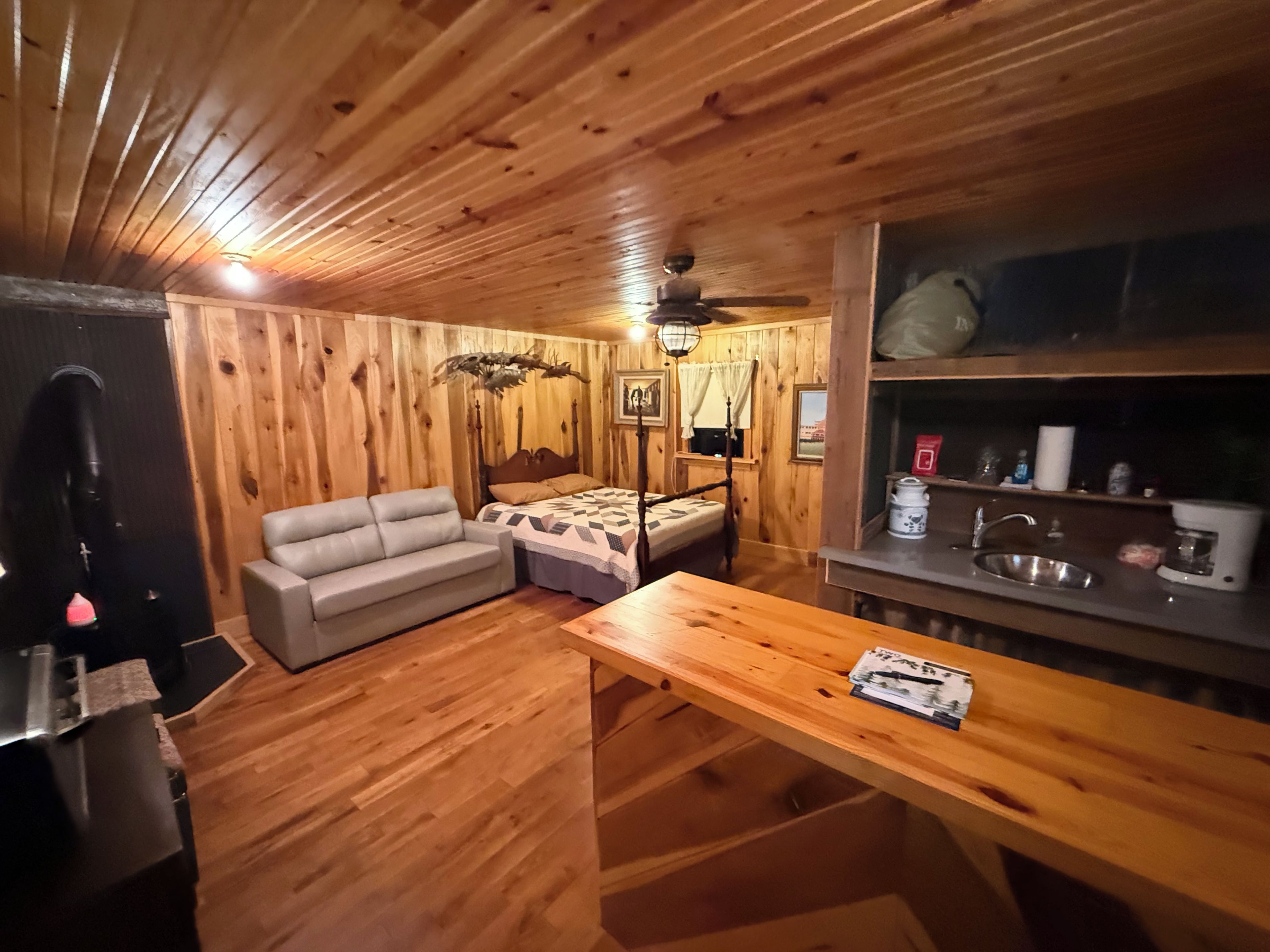 Interior de cabana de madeira com cama, sofá, mesa de jantar e cozinha compacta.