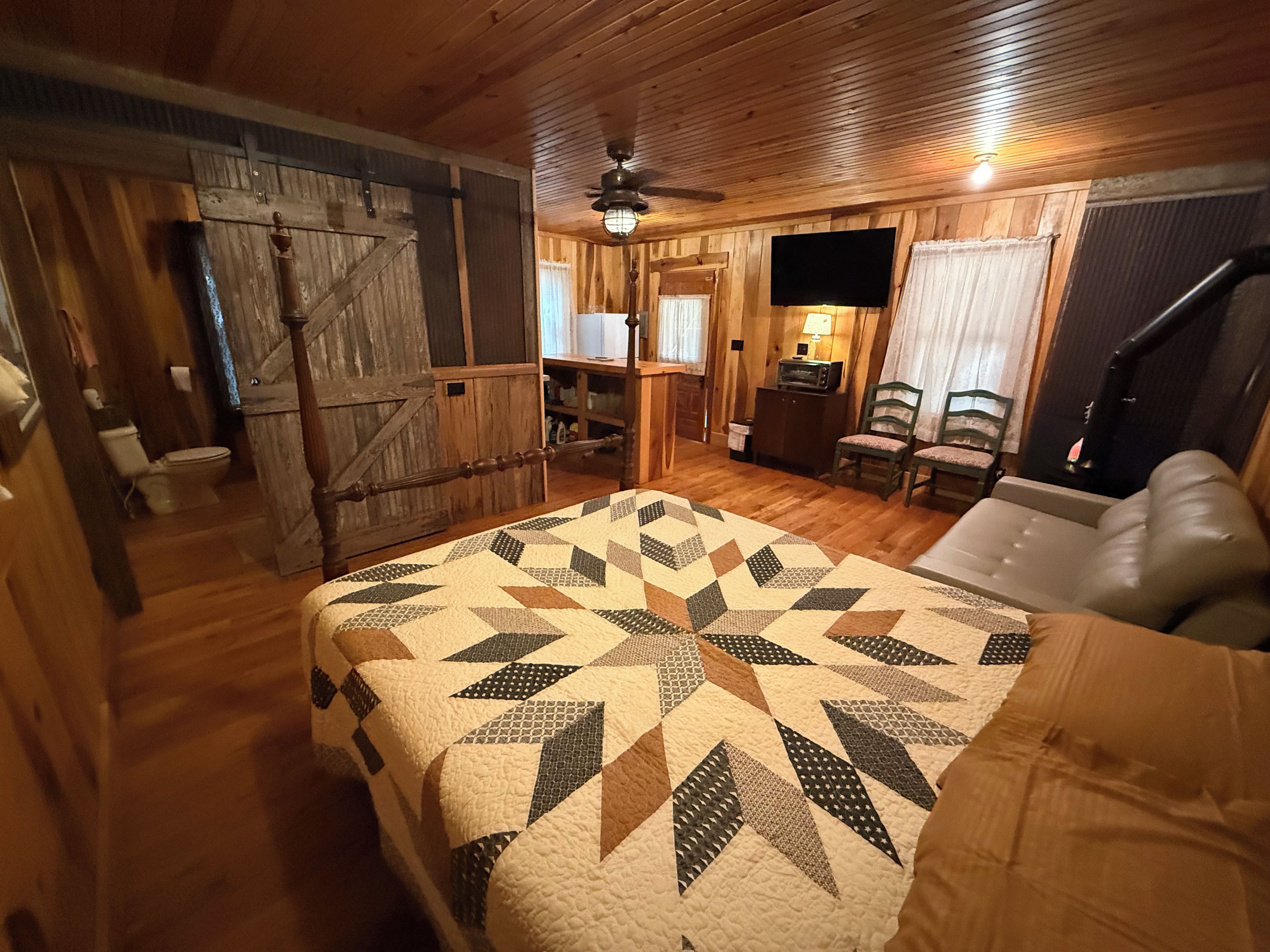 Una camera rustica con un letto, una scrivania, una sedia, una televisione e una ventola a soffitto.