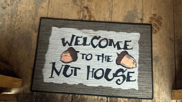 A wooden floor with a welcome mat that reads 'WELCOME TO THE NUT HOUSE' and a yellow toy in the background.